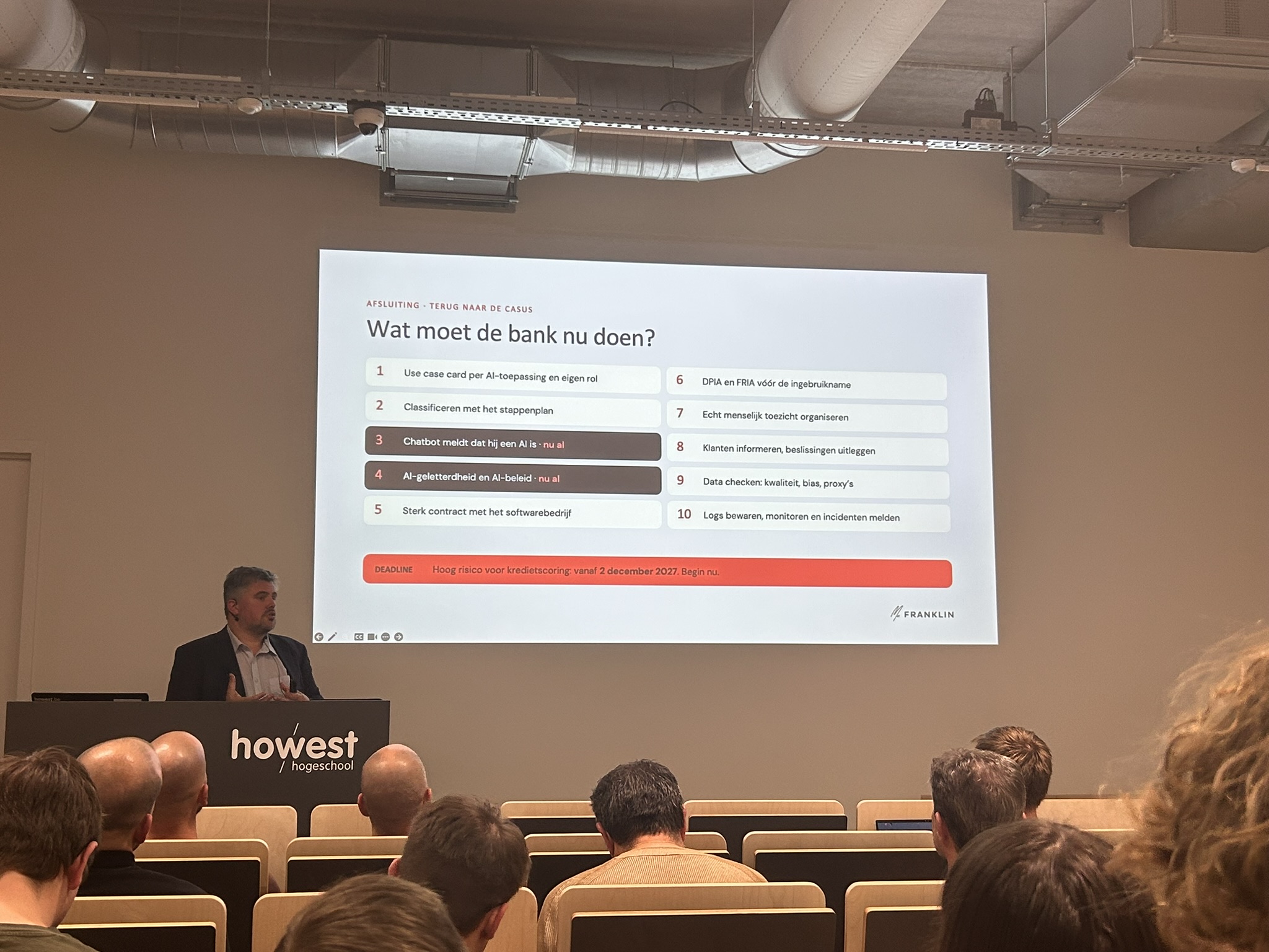 De spreker bij Howest tijdens de presentatie over de AI Act, met de afsluitende bankcasus op het scherm